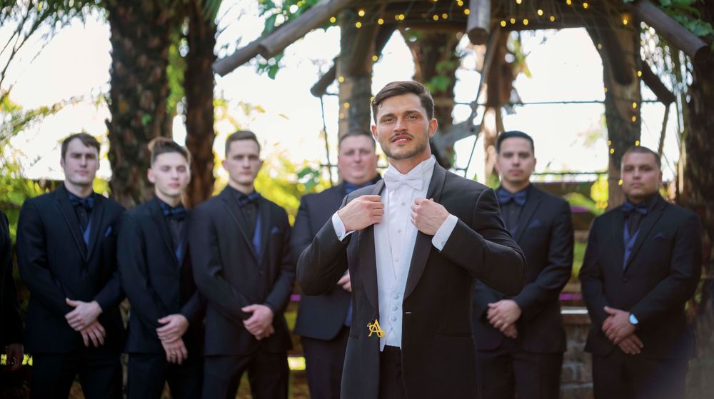 A formal wedding party wearing black suits with the groom adjusting his bowtie.