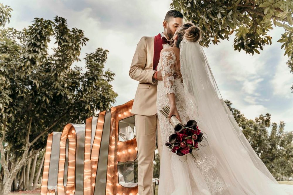 A wedding couple poses in front of illuminated LOVE letters during golden hour.