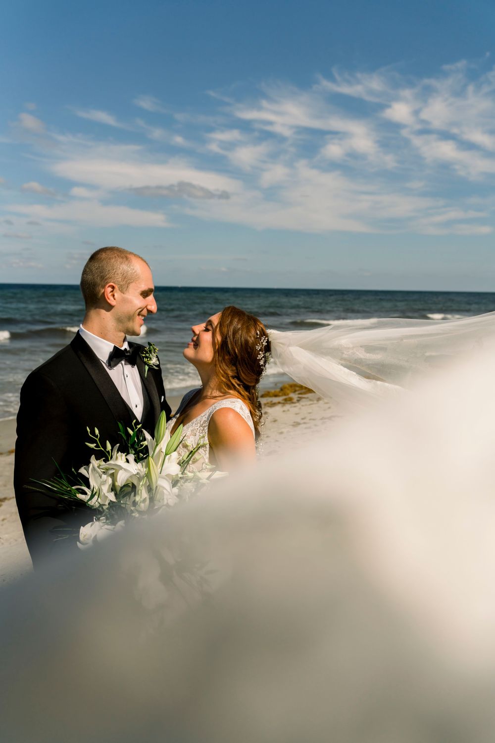 A beachside wedding portrait with flowing veil and ocean backdrop.