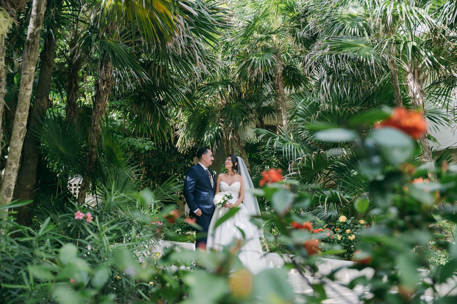 A couple shares a romantic moment surrounded by lush tropical greenery and vibrant flowers.
