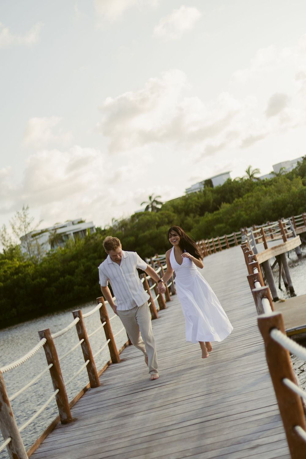 Happy couple holding hands and walking along a wooden boardwalk over tropical waters.