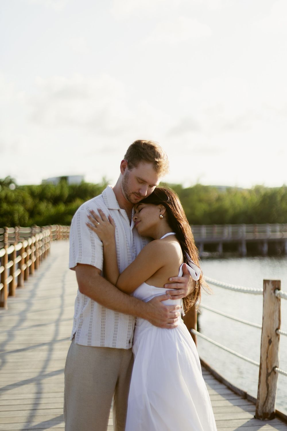 Couple sharing a warm embrace on a wooden boardwalk with tropical greenery in the background.