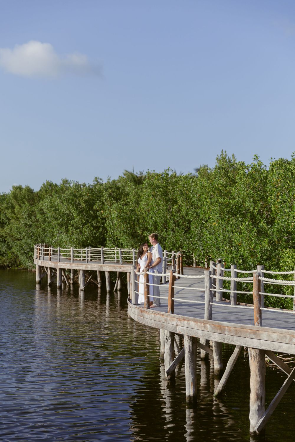 Couple standing together on an elevated wooden boardwalk overlooking a tropical mangrove waterway.