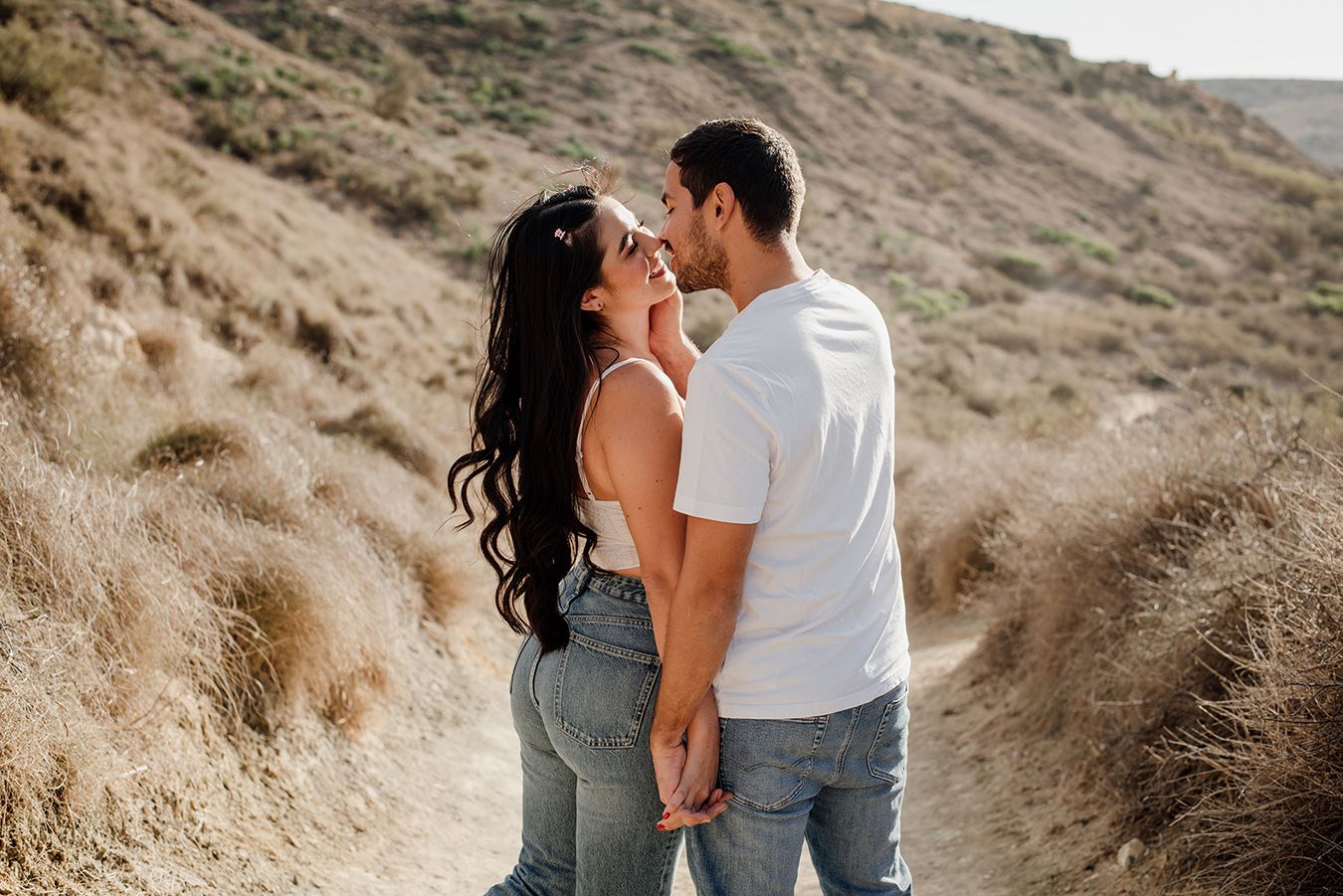 Couple holding hands and sharing a romantic moment on a scenic hiking trail with golden dry grass hills.