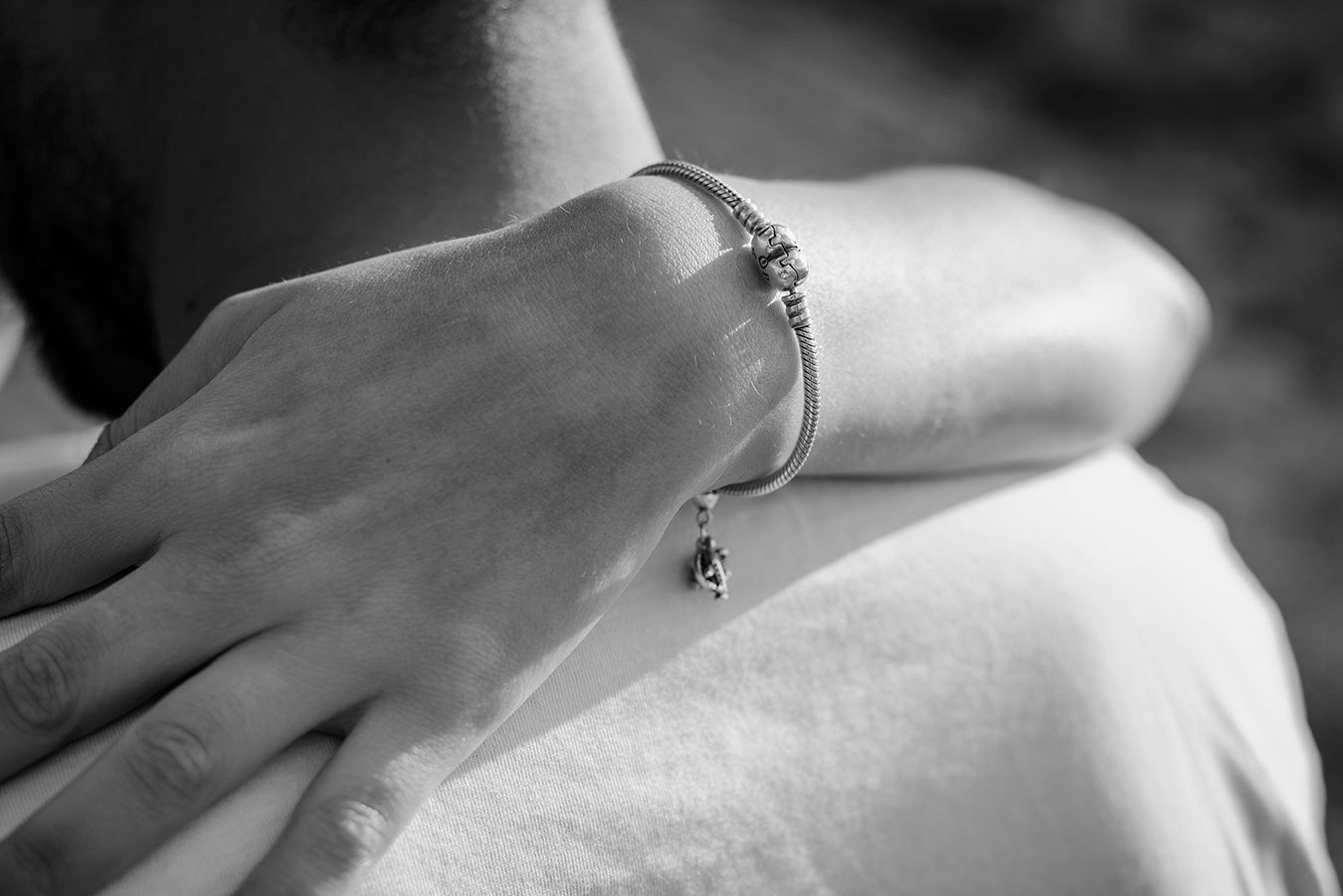Close-up of a silver charm bracelet with a delicate pendant on a woman's wrist, black and white photo.