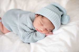 Newborn baby sleeping peacefully in a soft blue knit swaddle and matching hat on white blanket at Fort Sanders Medical Center in Knoxville.