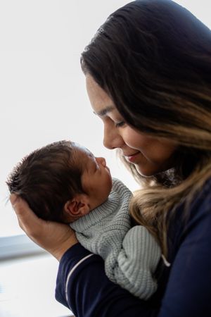 A mother tenderly holds her newborn baby close, gazing lovingly at the infant wrapped in a cozy gray knit blanket at Fort Sanders.