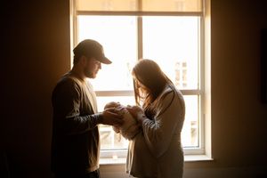 Couple standing by a sunlit window holding their newborn baby in a warm, intimate moment at Tennova North Knoxville Medical Center.