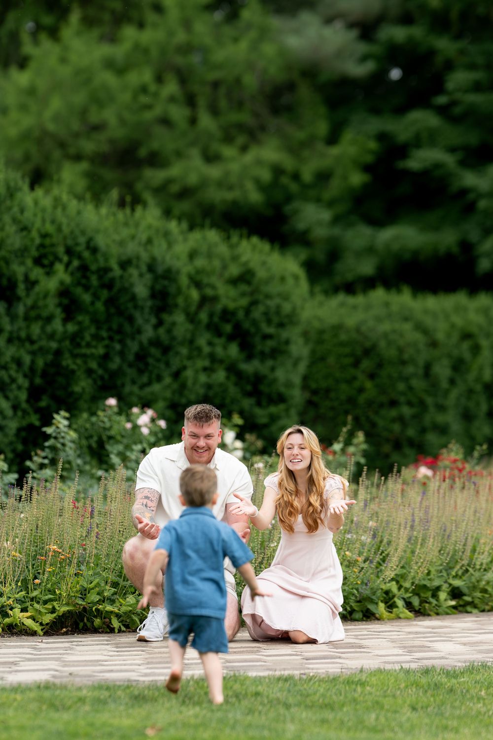 Happy family with young child running toward parents in a lush green garden with colorful flowers.