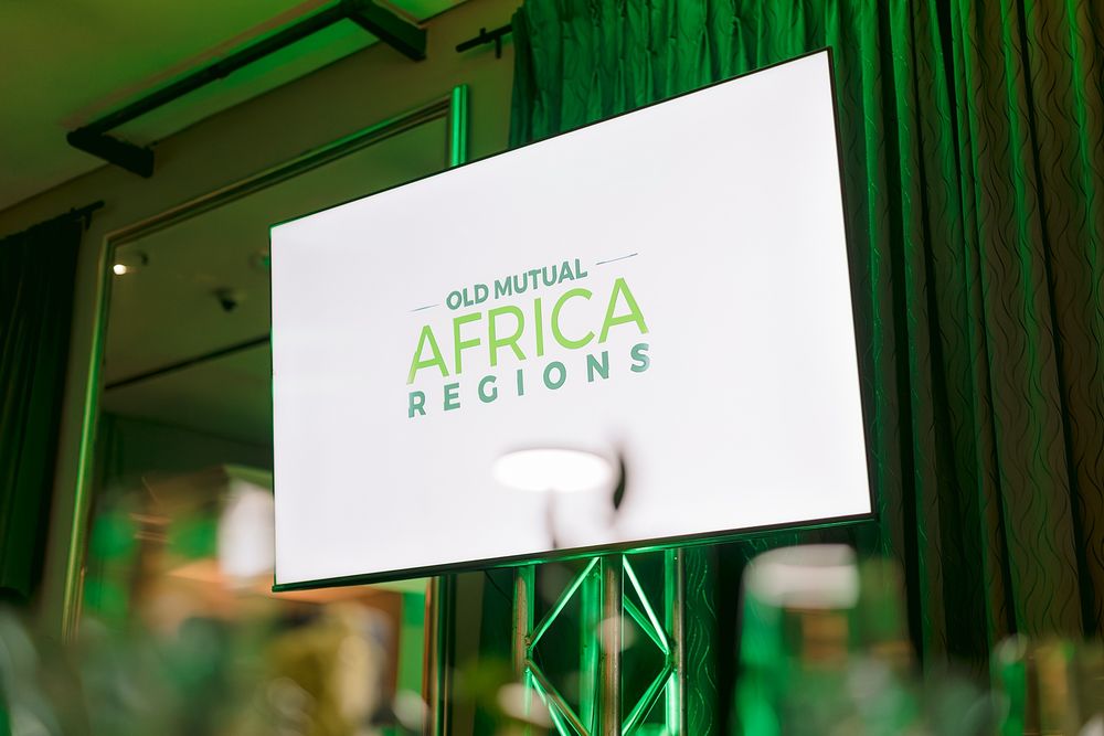 Old Mutual Africa Regions logo displayed on a white screen at a corporate event with green curtain backdrop.
