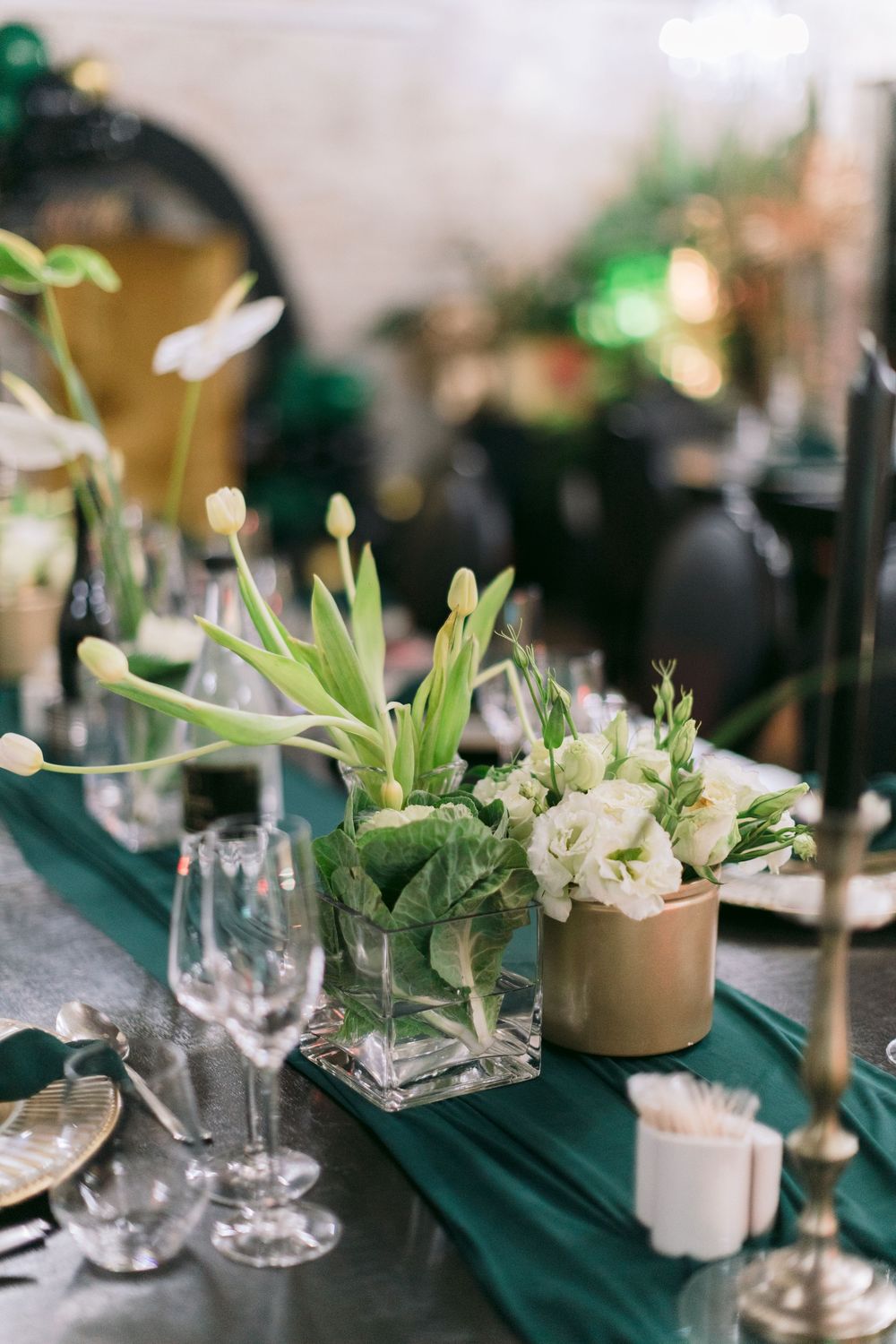 Formal table centerpiece with white tulips, green runner, gold vase, and crystal glassware.