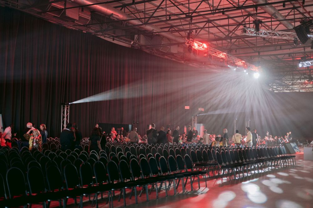 Dramatic conference hall setup with rows of black chairs, red stage lighting, and spotlight beams through fog.