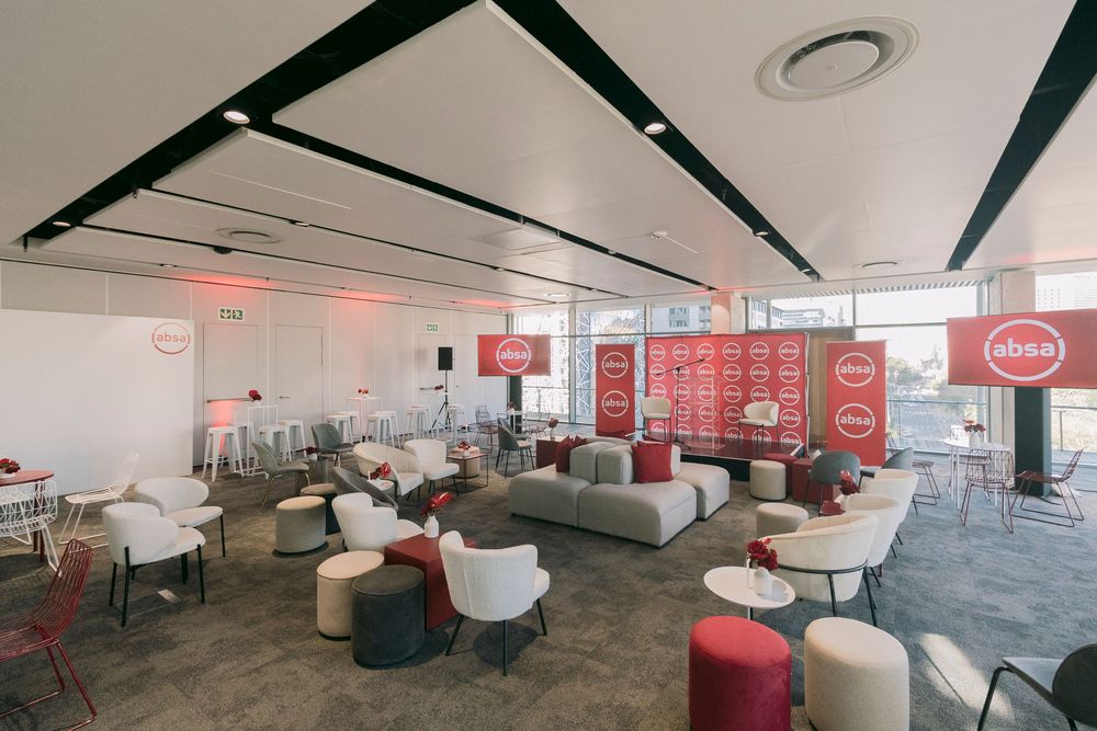 Modern corporate lounge with red Absa branding, white sofas, and stylish seating arrangements in a bright event space.