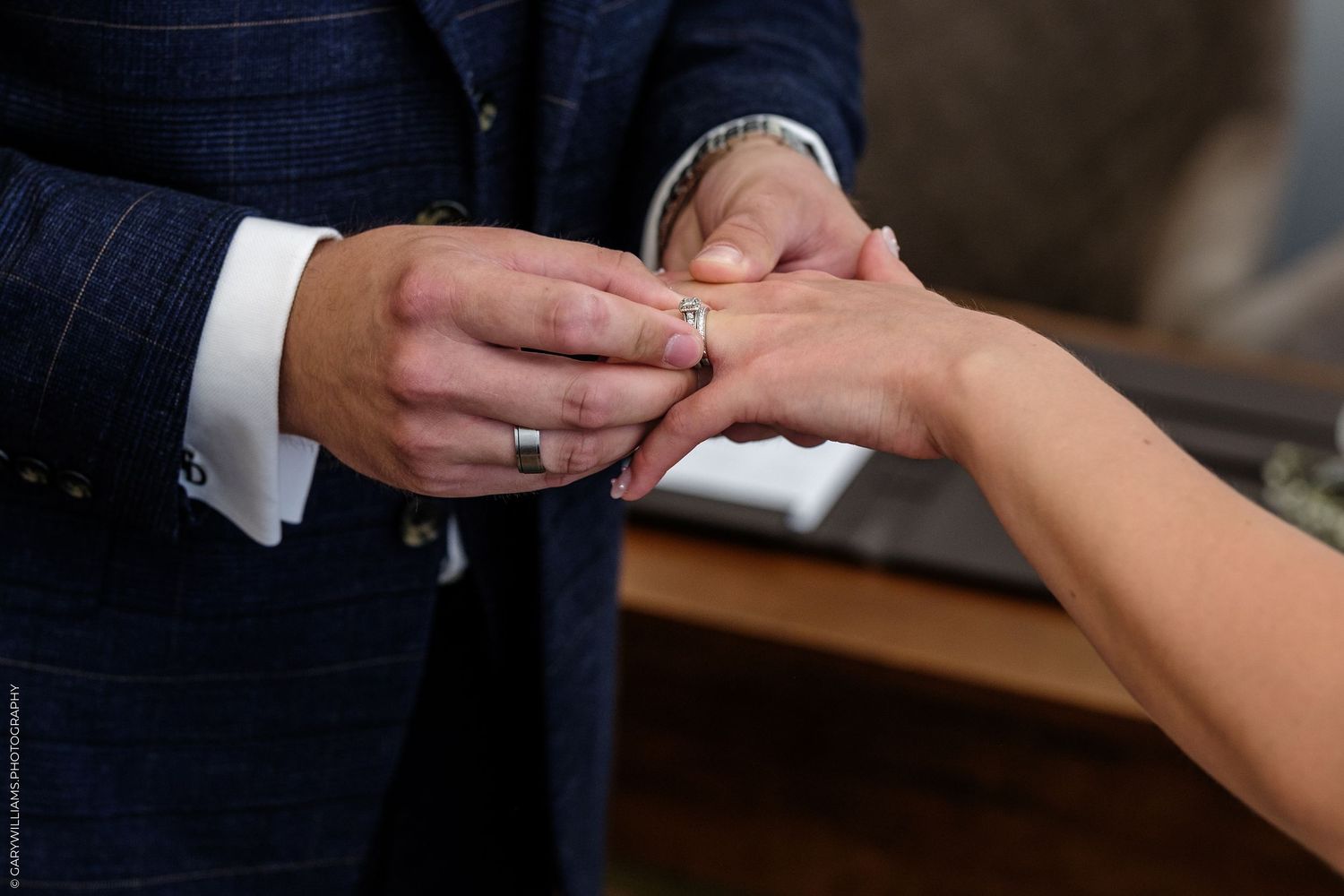 Groom placing wedding ring on bride's finger during ring exchange ceremony.