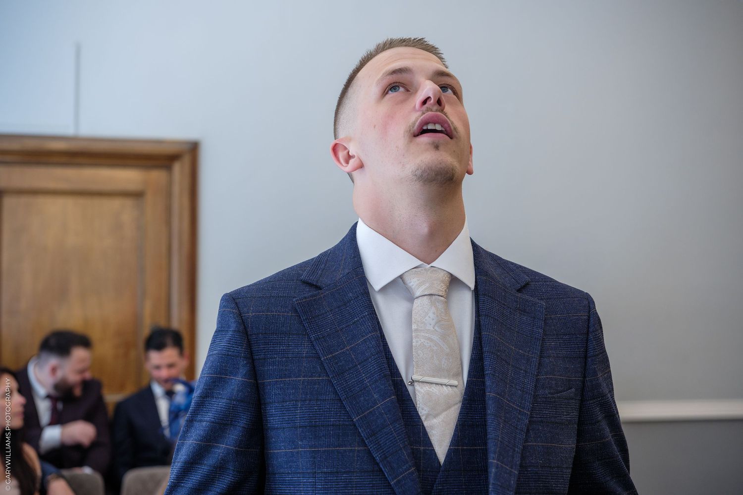Man in blue suit and white tie looking upward at a formal indoor event.