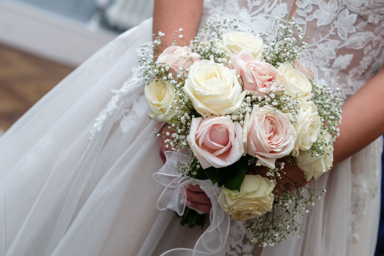Bride holding a wedding bouquet of pink and white roses with baby's breath in a lace gown.