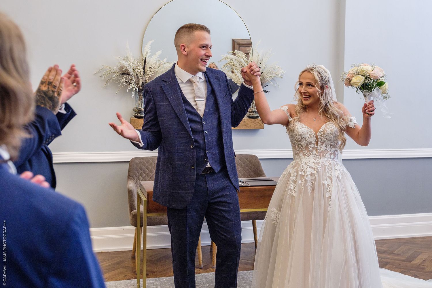 Newlyweds celebrate with raised hands as guests applaud after their wedding ceremony.