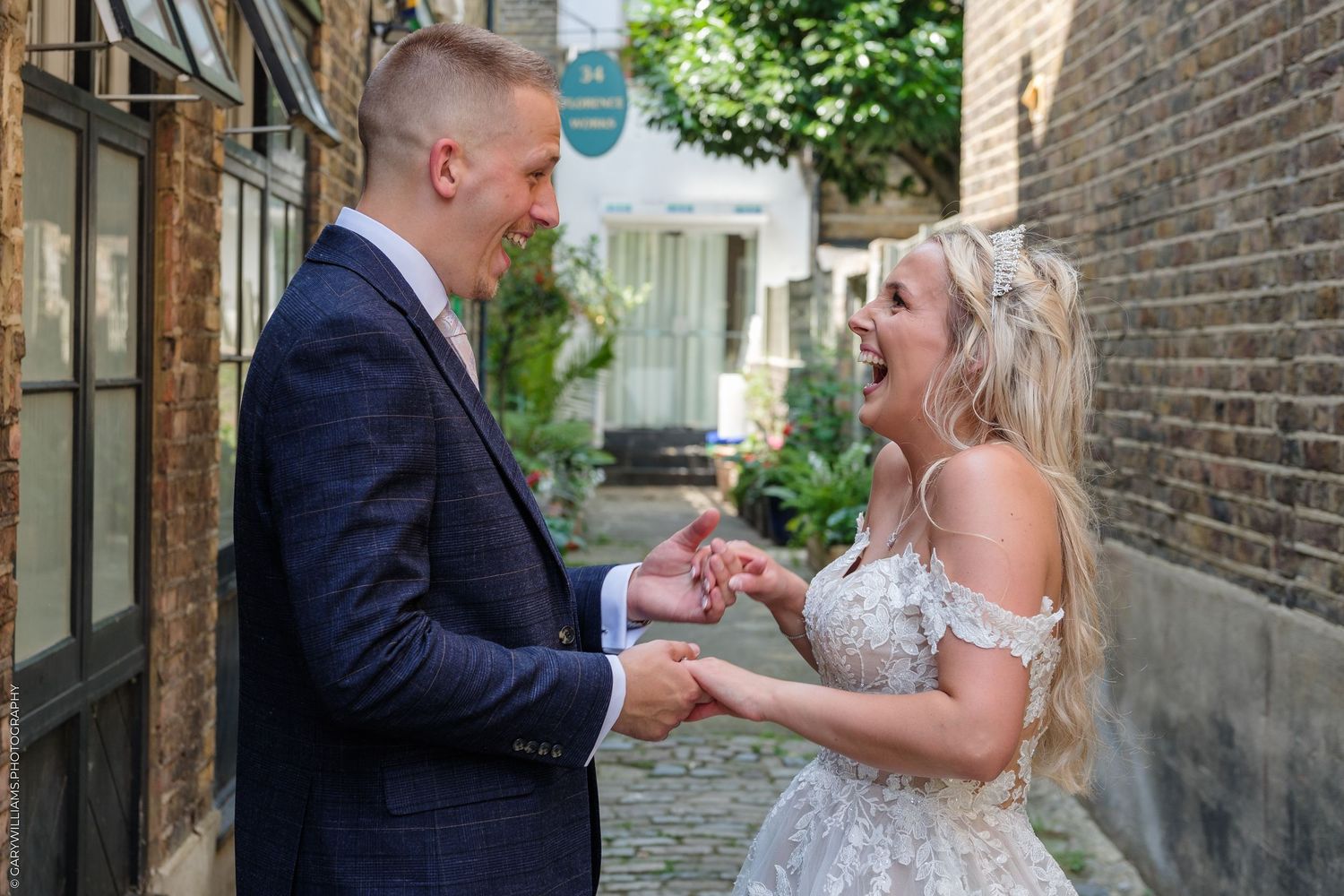 A joyful bride and groom hold hands and laugh together in a charming brick alleyway on their wedding day.