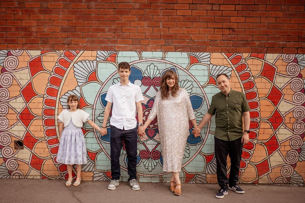 Family group poses against a vibrant red brick wall with geometric mural artwork.