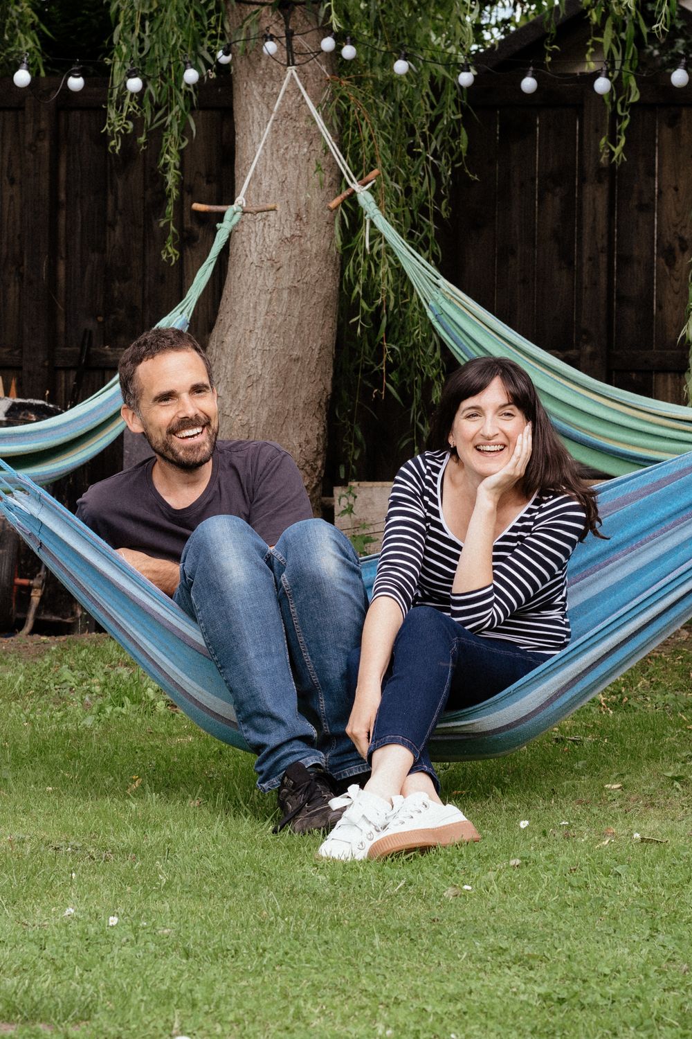 Couple relaxing together in striped hammock under string lights in backyard.