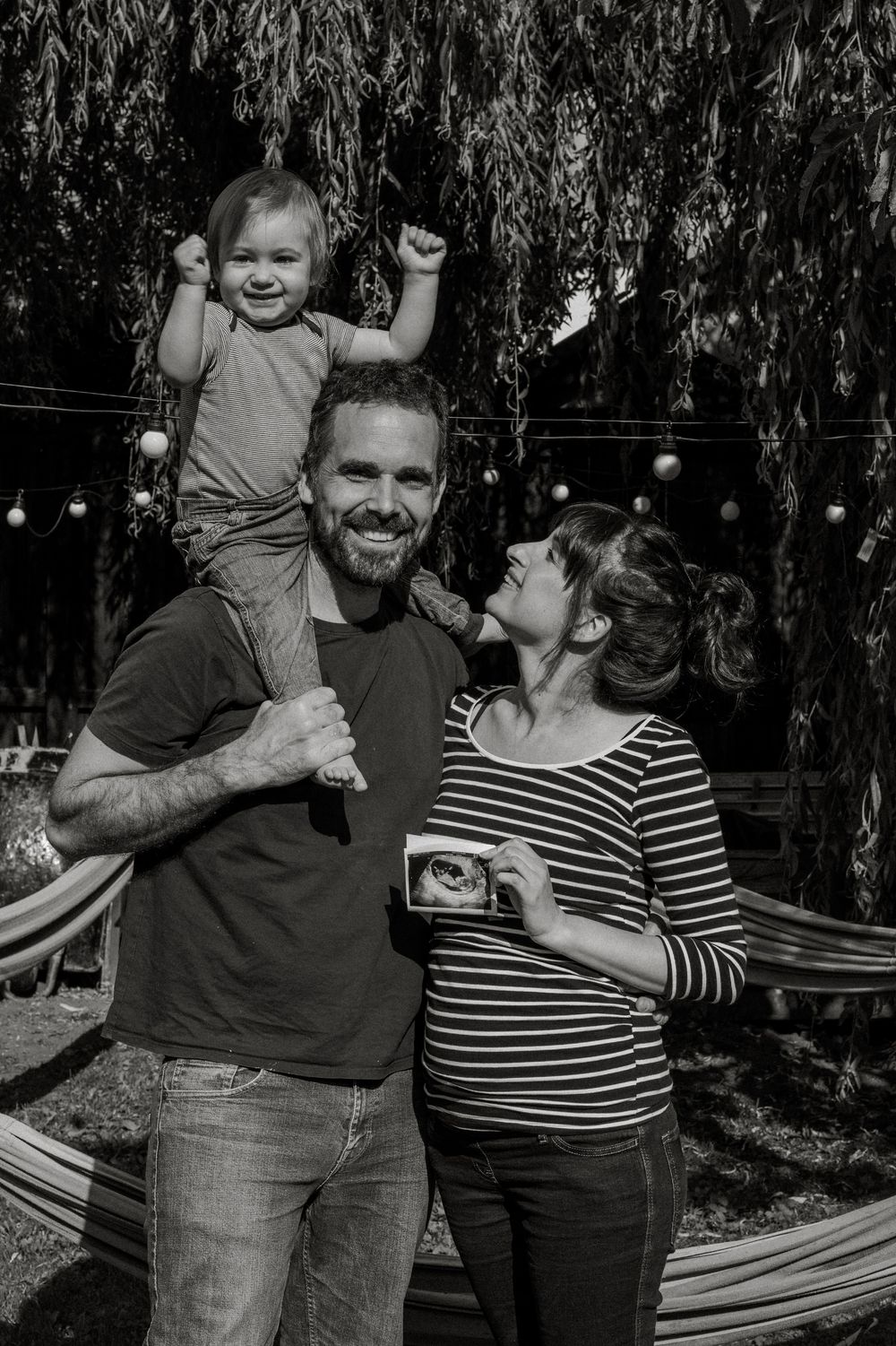 Family sharing candid moments together near hammock in backyard garden setting.