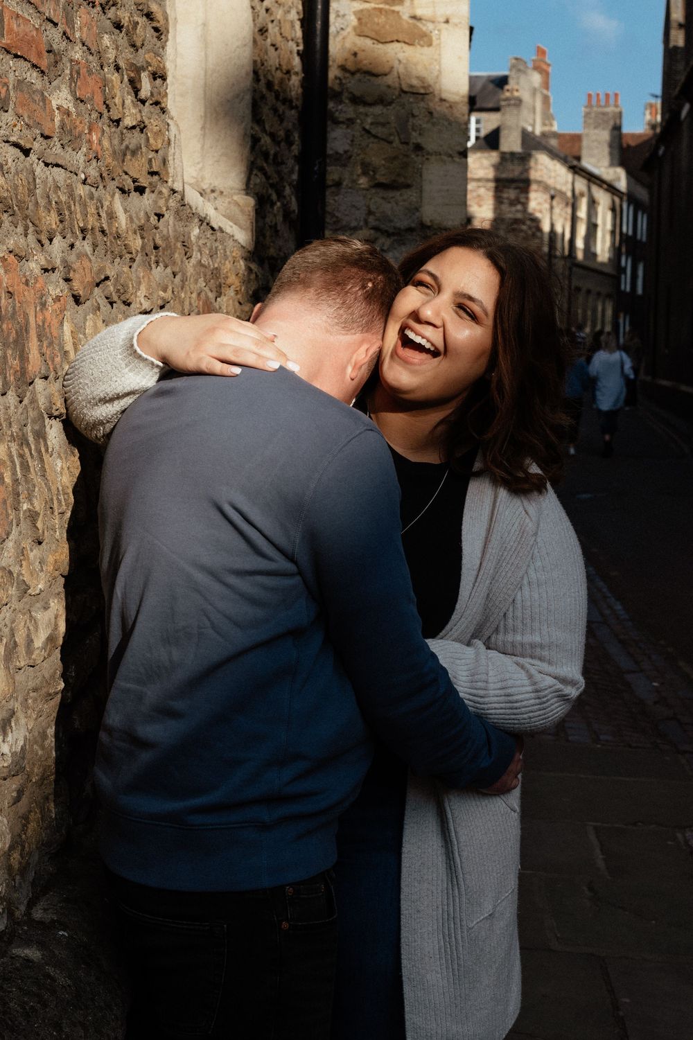 Candid laughing moment between couple against stone wall background.