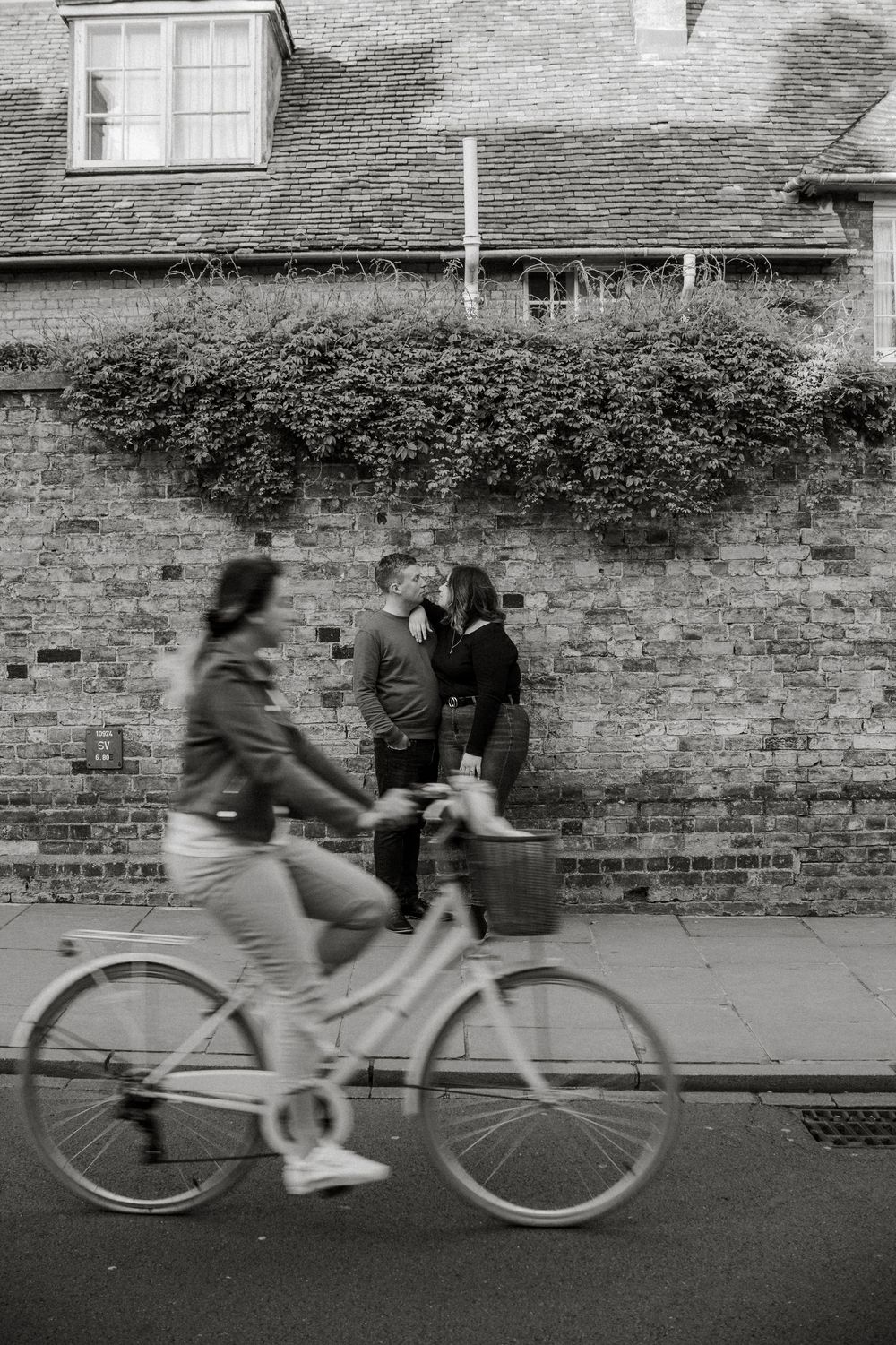 Motion blur photograph of cyclists passing brick wall in black and white.