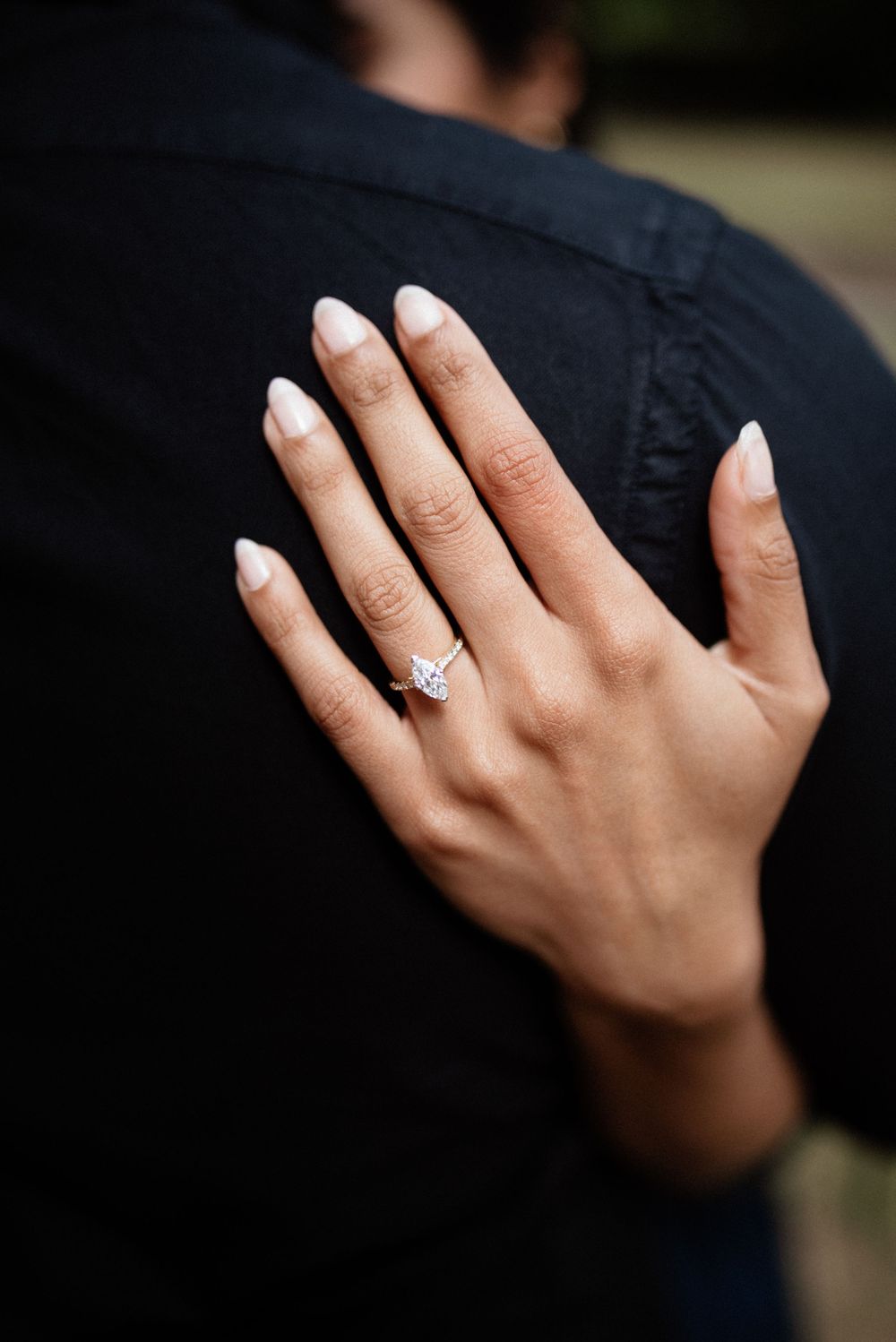 Close-up view of a sparkling engagement ring on a hand against dark fabric.
