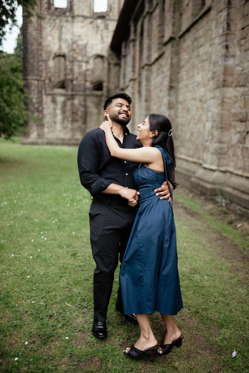 Romantic couple sharing intimate moments against historic stone wall backdrop.