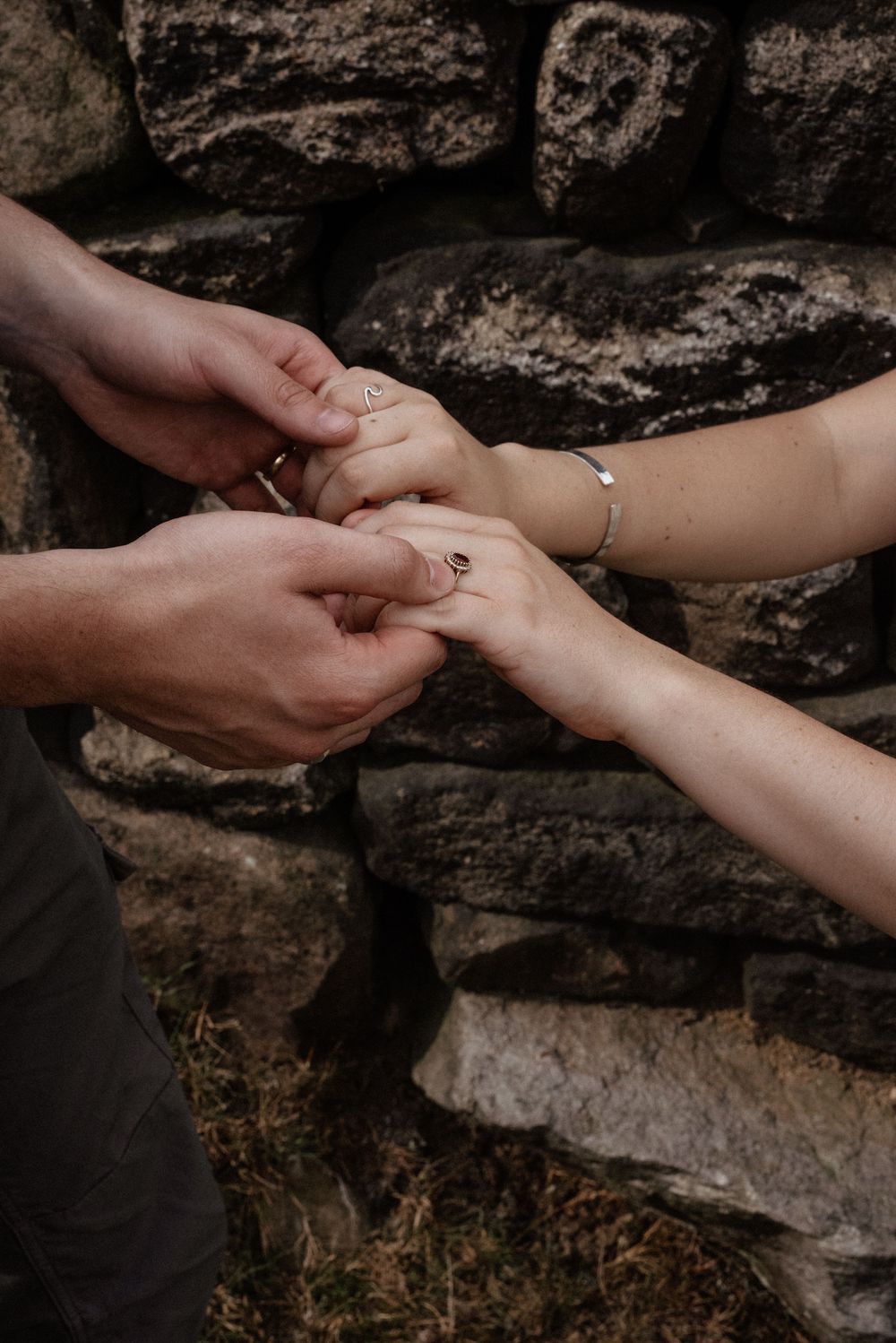 Close-up sequence of hands exchanging a ring against a textured stone background.