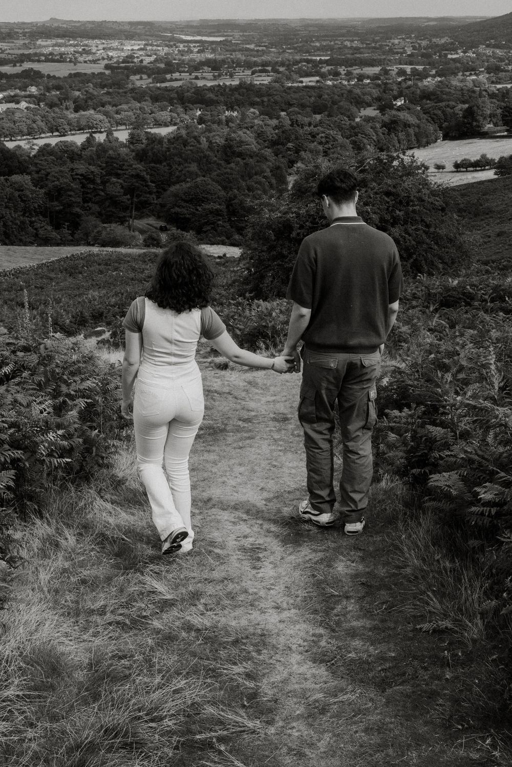 Couple walking together on a hilltop path overlooking a scenic valley landscape.