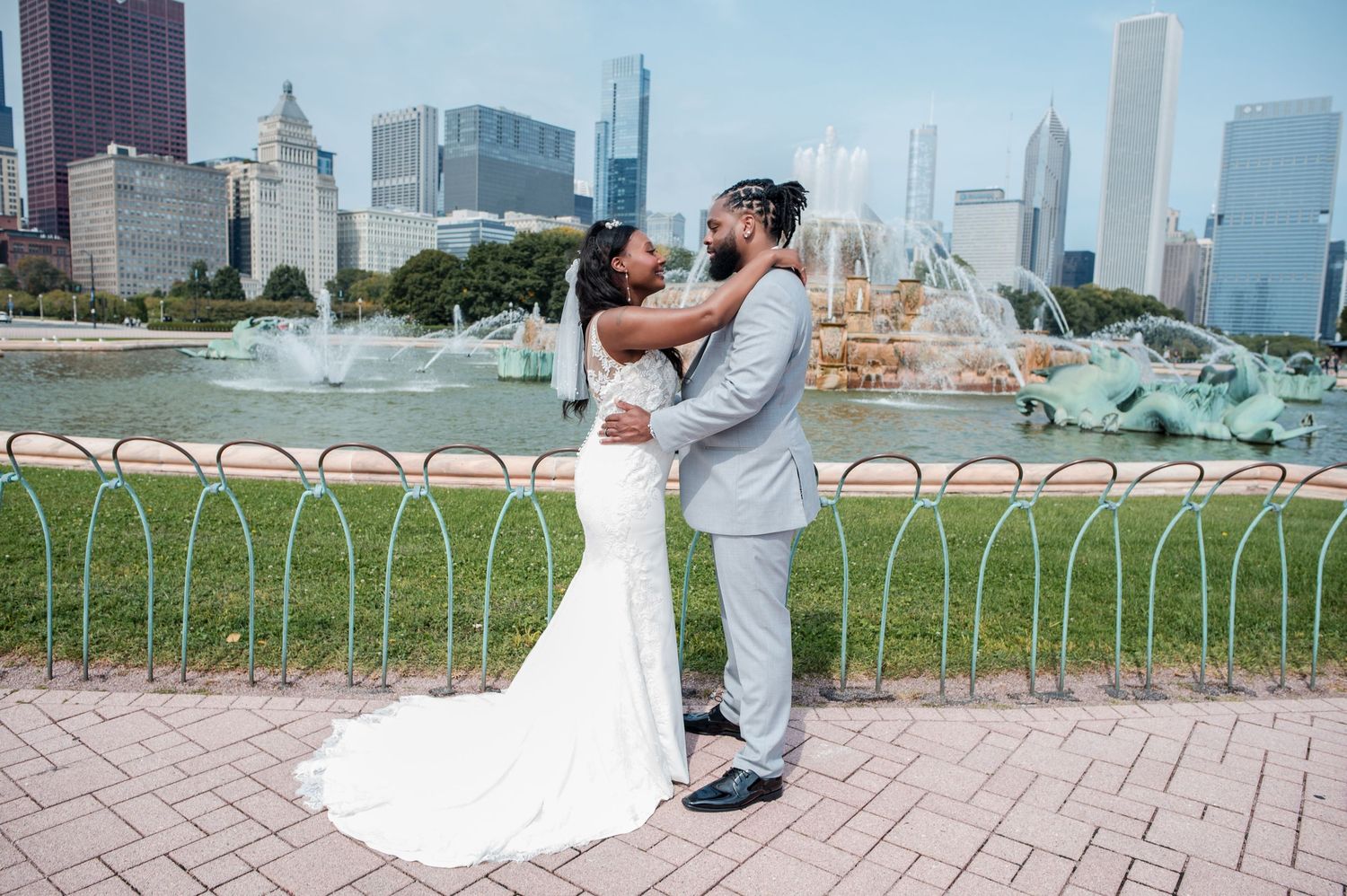A couple embraces romantically in front of Buckingham Fountain with the Chicago skyline in the background.