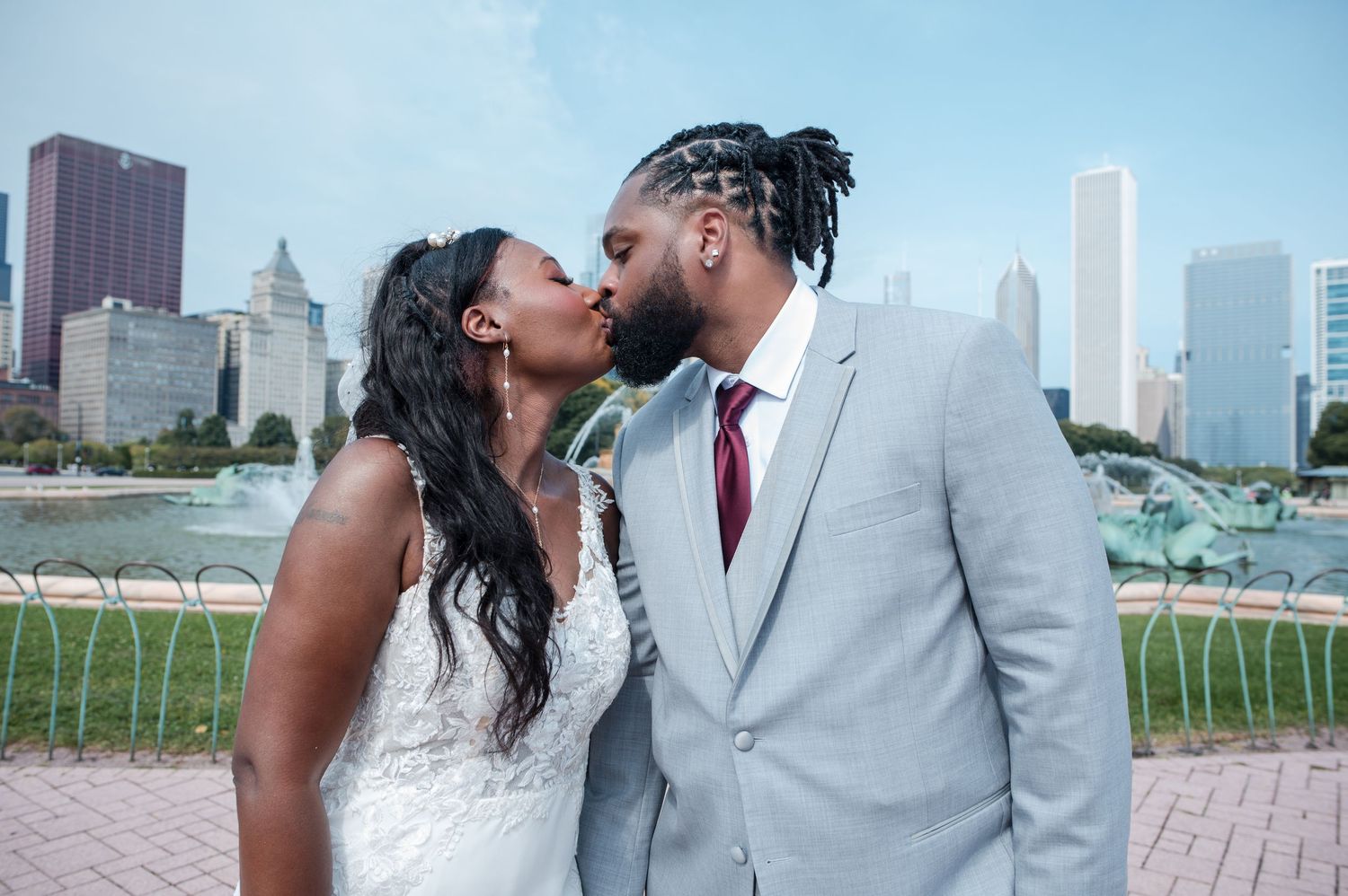 Newlyweds share a kiss in front of Buckingham Fountain with Chicago skyline in the background.