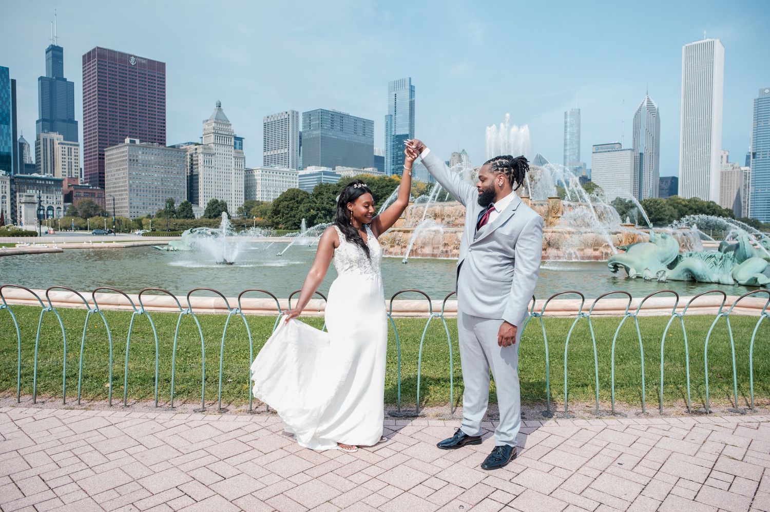 Newlywed couple celebrating in front of Buckingham Fountain with Chicago skyline backdrop on their wedding day.