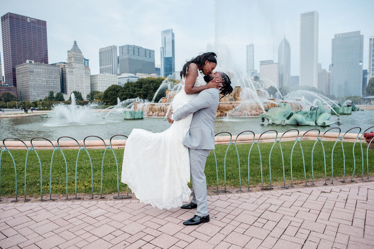 Couple sharing romantic dip kiss at Buckingham Fountain with Chicago skyline backdrop on wedding day.