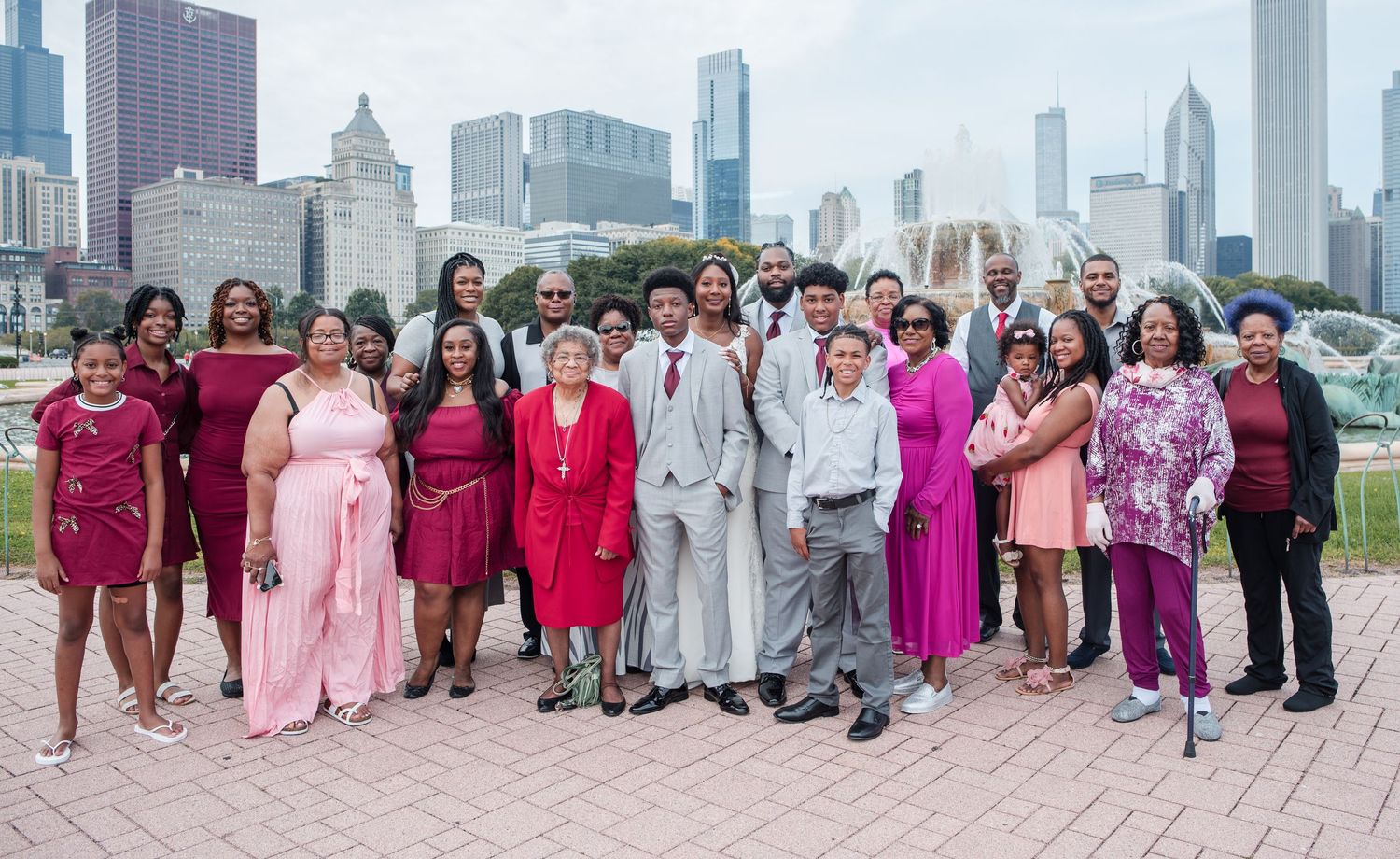 Large wedding party group photo in pink and burgundy attire with Chicago skyline backdrop.