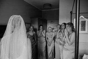 Black and white photo of bridesmaids reacting with joy and tears as bride reveals her wedding dress.