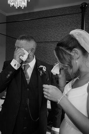 Black and white photo of emotional bride and groom crying on wedding day, wiping tears with handkerchiefs.