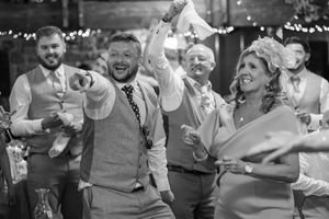 Guests celebrate and dance joyfully at a rustic barn wedding reception in black and white photo.