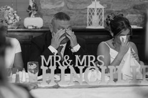 Emotional bride and groom crying at wedding reception table with Mr & Mrs sign in black and white photo.