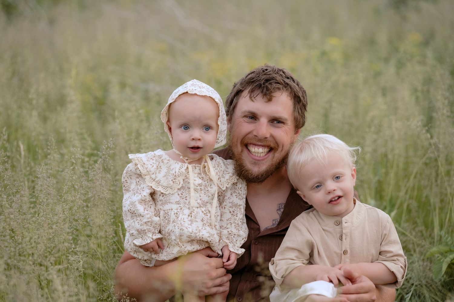 Dad holds toddler and baby while sitting in a grassy field for family photos in Hudson, WI.