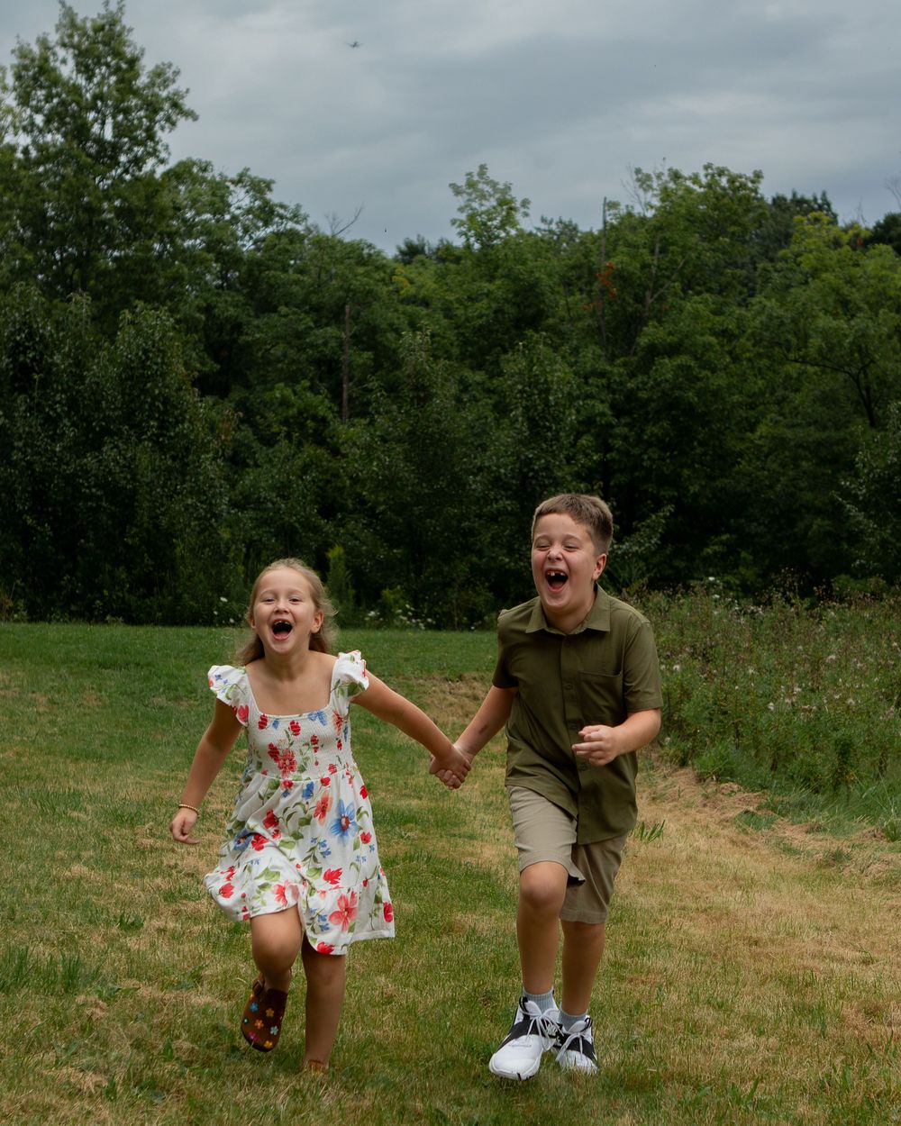 Brother and sister running through a field laughing in strongsville.