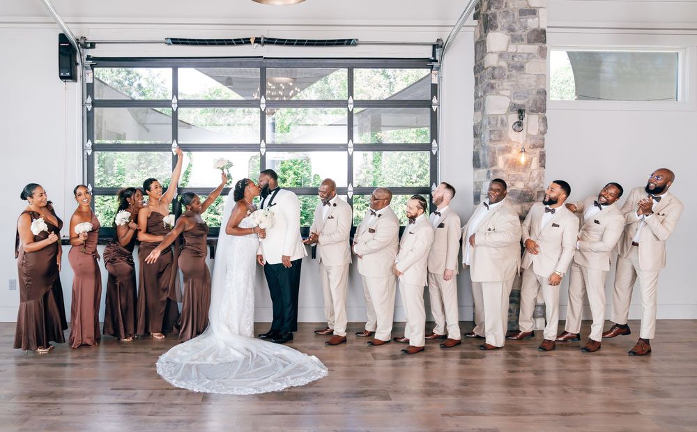 Wedding party celebrating in elegant venue, bridesmaids in brown gowns and groomsmen in cream suits flanking bride and groom.