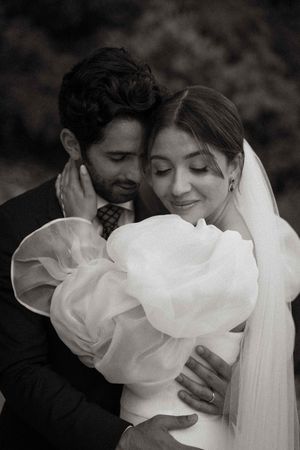 A tender black and white portrait of newlyweds embracing, with the bride wearing a dramatic ruffled dress.