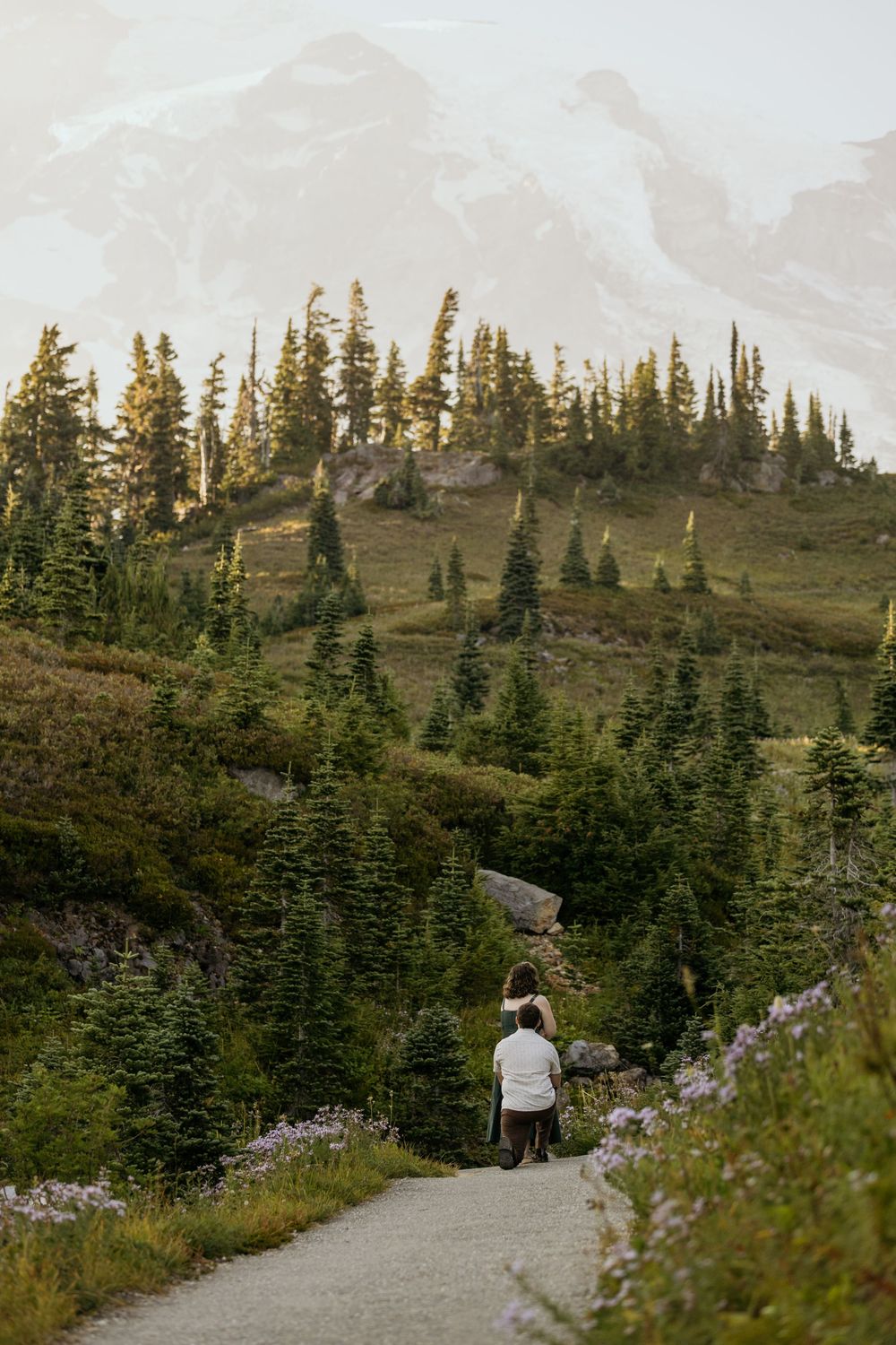 Hiker walking on a paved trail through evergreen forest with mountain views at Mount Rainier National Park.