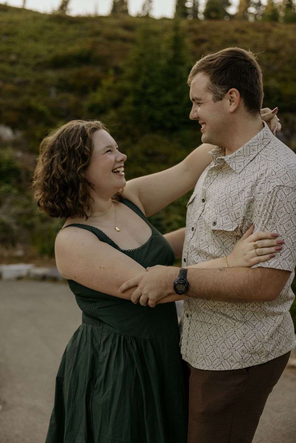 Happy couple laughing and dancing outdoors with lush green hillside in the background.