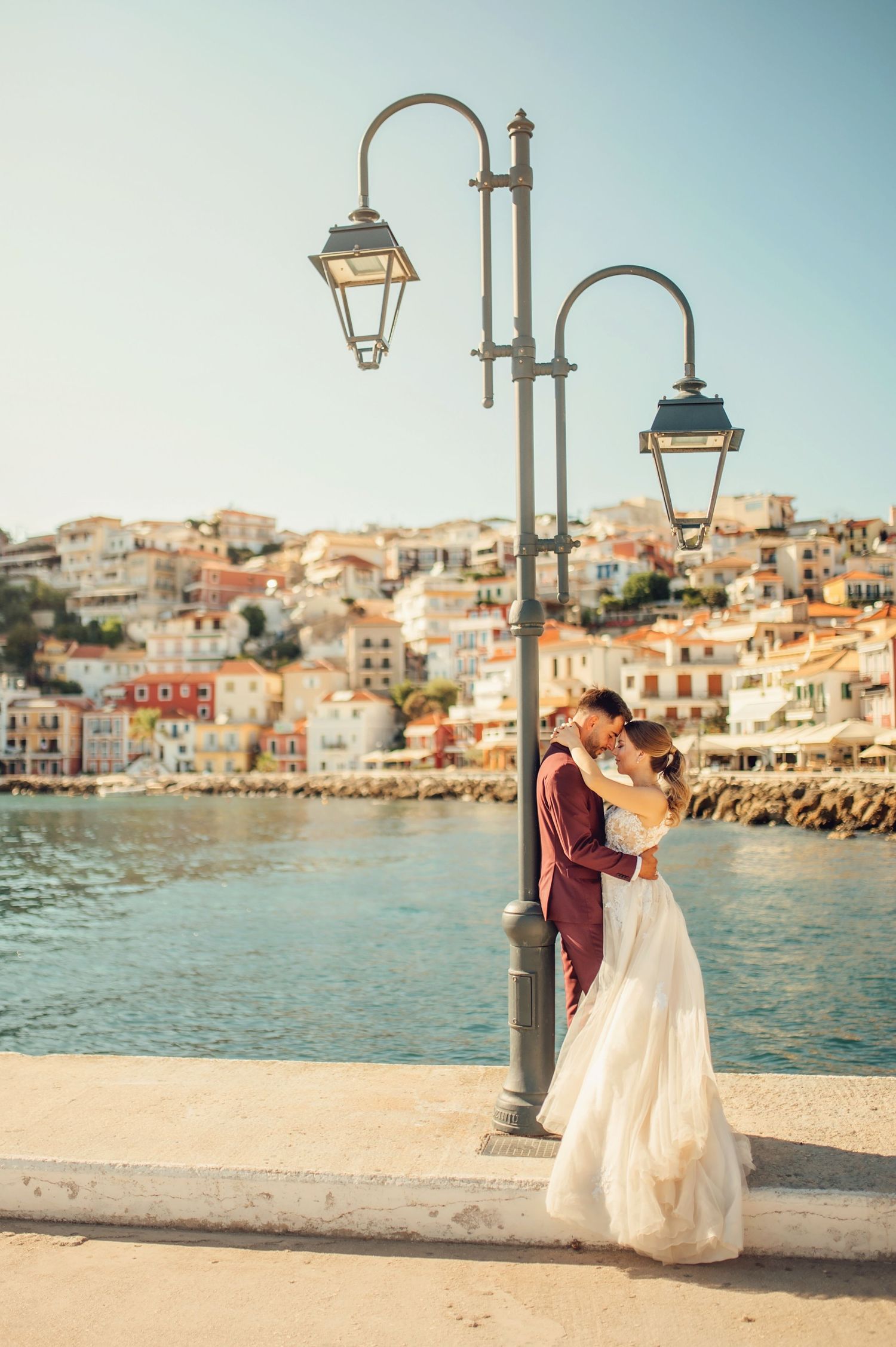 A bride and groom embrace romantically on a sandy beach at sunset, surrounded by white and dark horses.
