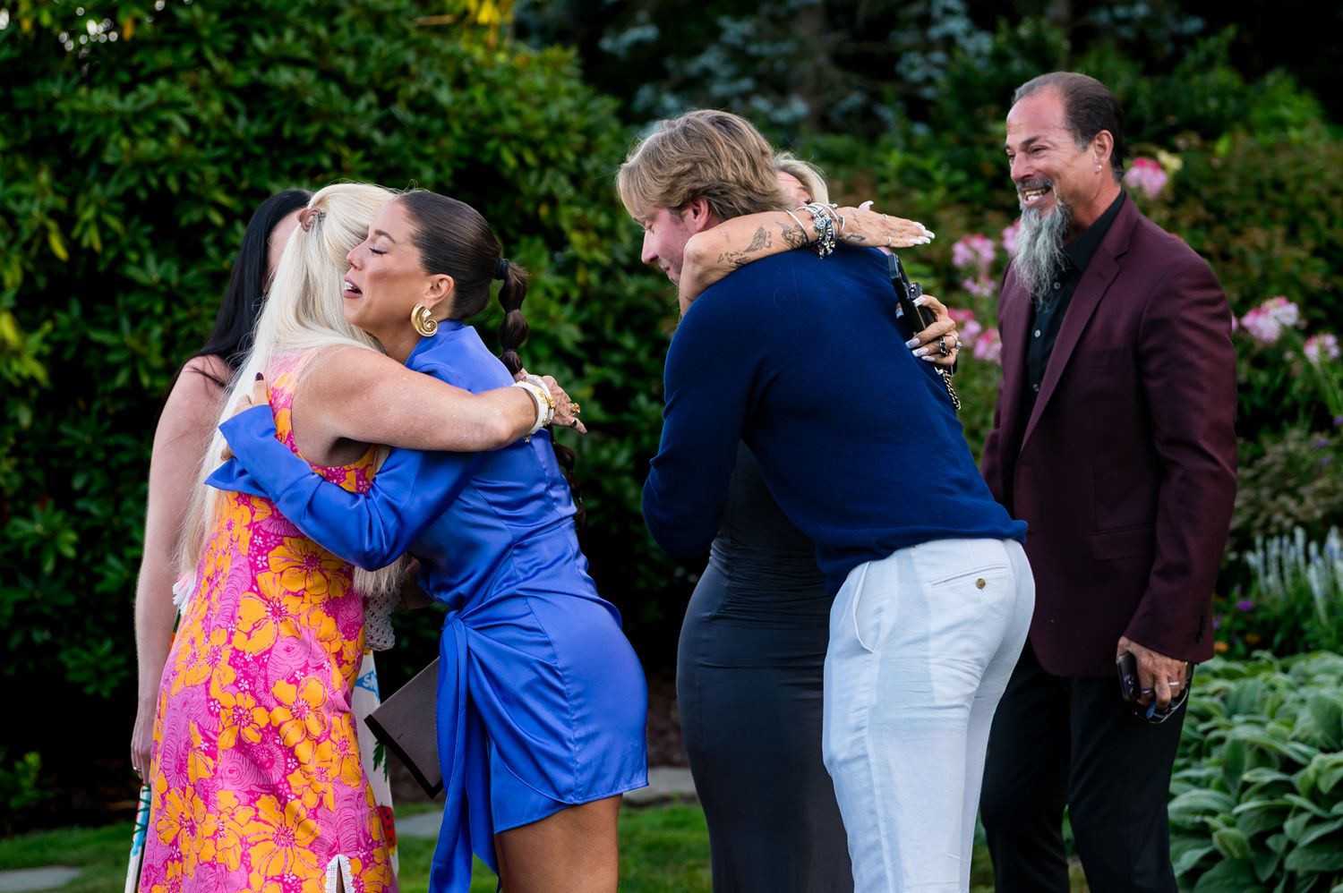 Two couples exchanging warm hugs outdoors in garden setting during a festive celebration gathering.