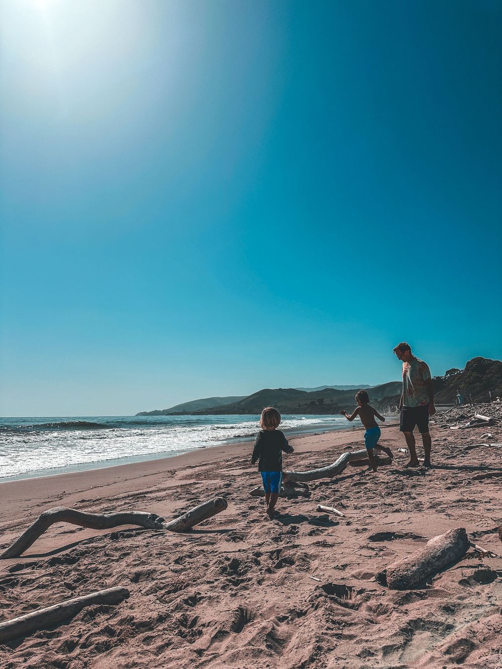 Family enjoying sunny beach day with ocean waves and clear blue sky in background.