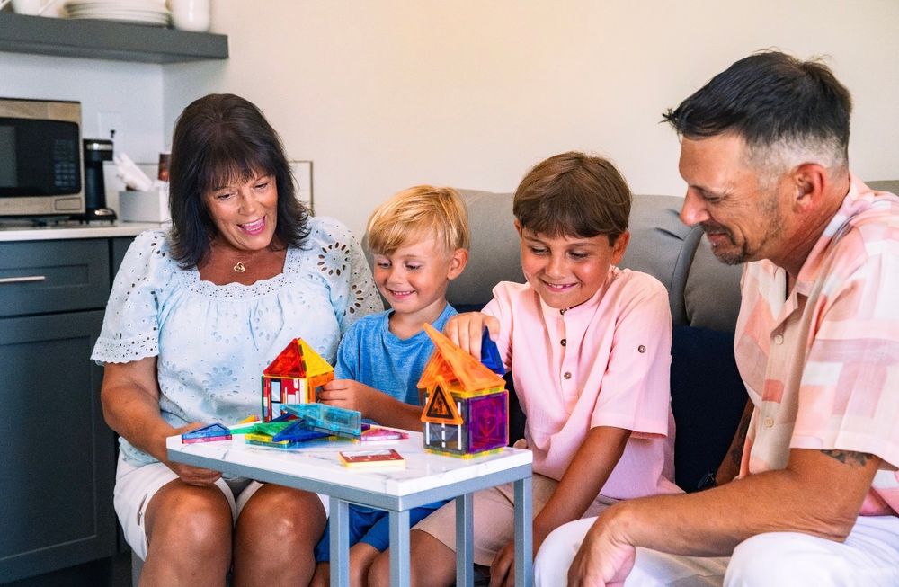 Grandparents and two grandchildren playing with colorful building blocks in a cottage living area.